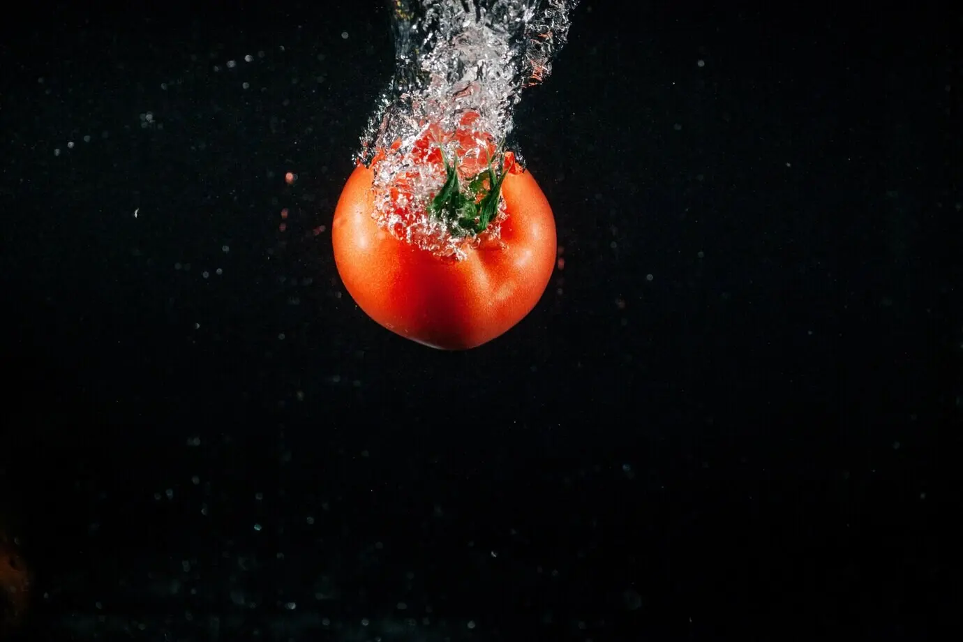 Eine frische große Tomate fällt ins Wasser und bildet Blasen.